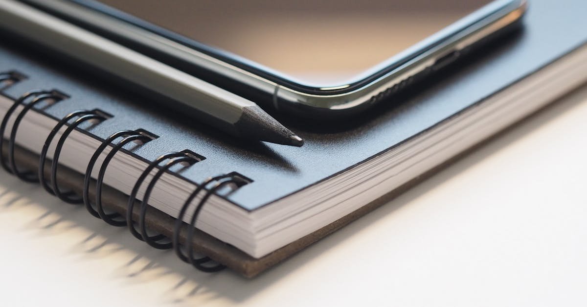 Close-up of a spiral notebook, smartphone, and pencil on a desk, highlighting modern workspace essentials.